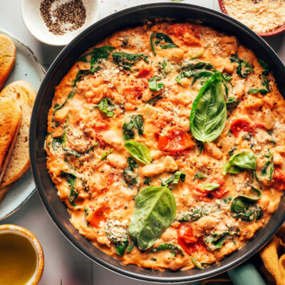 Skillet of Italian white beans with burst tomatoes, spinach, basil, and cashew cream