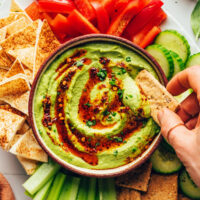 Dipping a cracker into a bowl of herby green goddess hummus