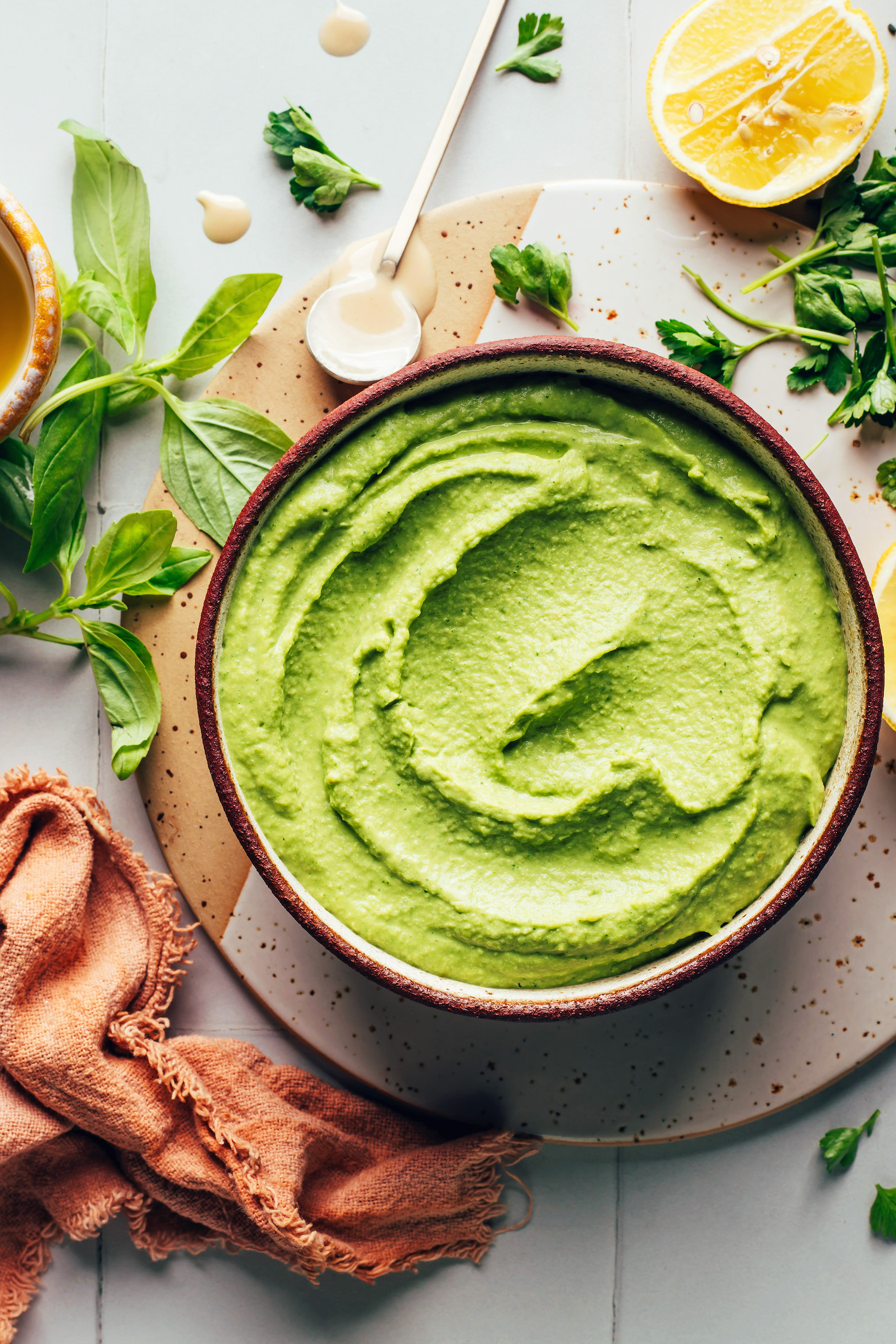 Vibrant green goddess hummus in a bowl surrounded by fresh herbs and lemon