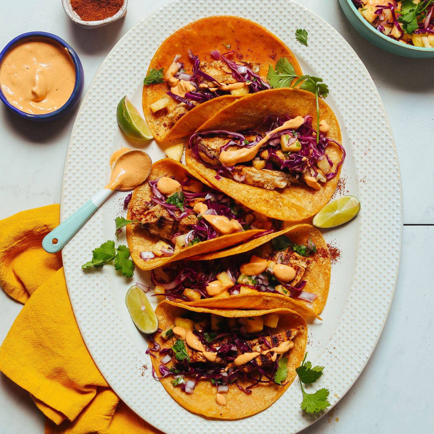 Spoonful of dairy-free chipotle aioli resting on a platter of Grilled Fish Tacos with Pineapple Cabbage Slaw