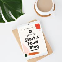 A cup of coffee sitting next to an ipad resting on a wooden block with first page of the email course How to Start A Food Blog by Minimalist Baker