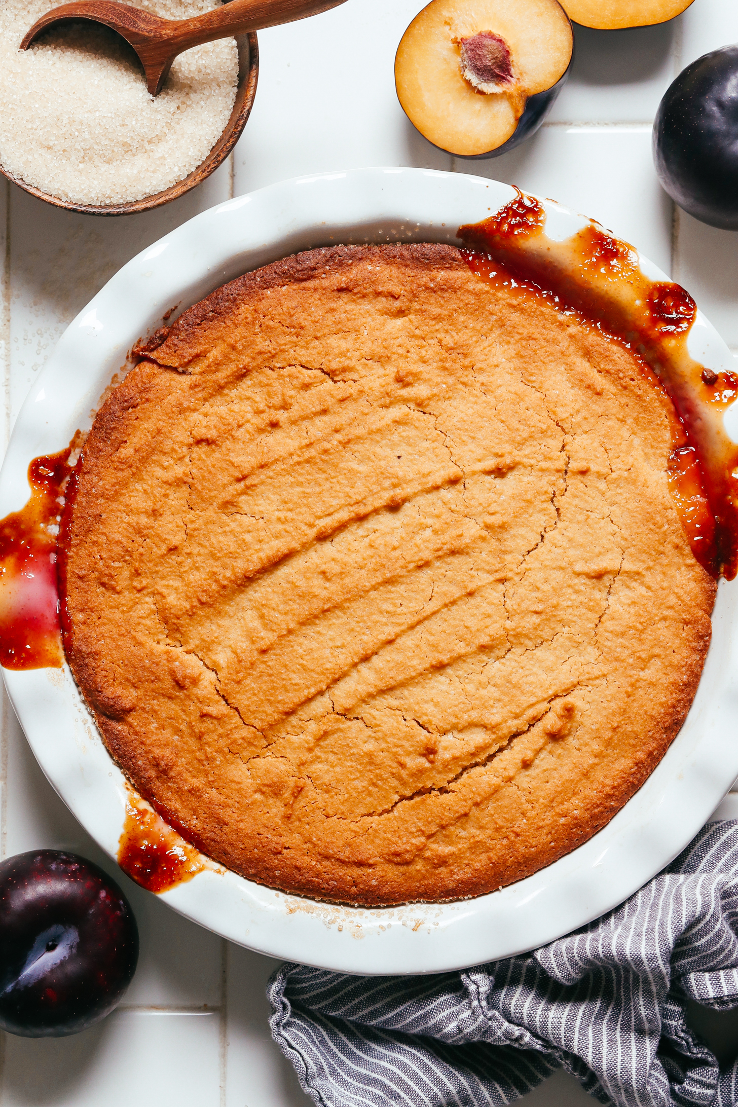 Freshly baked plum upside down cake with a golden brown top and bubbly fruit marking the sides of a pie pan