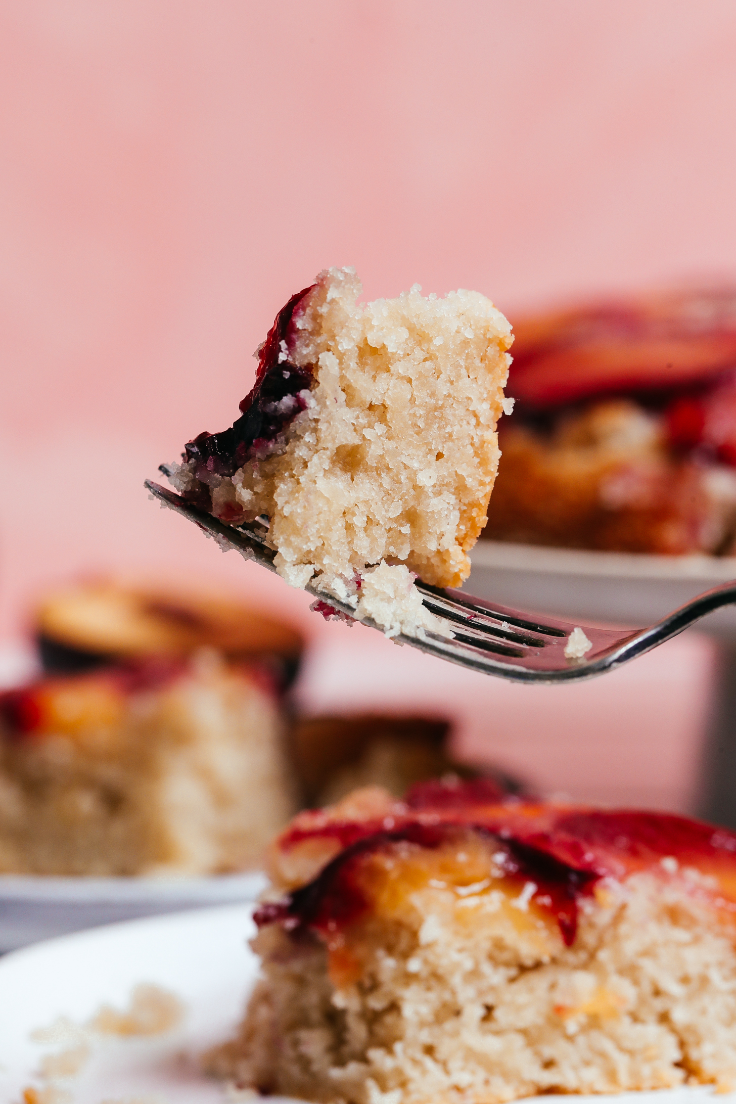 Bite of plum almond cake on a fork with the rest of the slice on a plate behind it