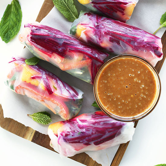 Parchment-lined cutting board with Rainbow Spring Rolls and a bowl of Ginger Peanut Sauce