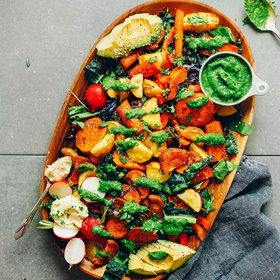 Wood platter filled with Roasted Vegetable Salad drizzled with chimichurri