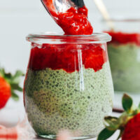 Using a spoon to top a jar of matcha chia pudding with strawberry compote
