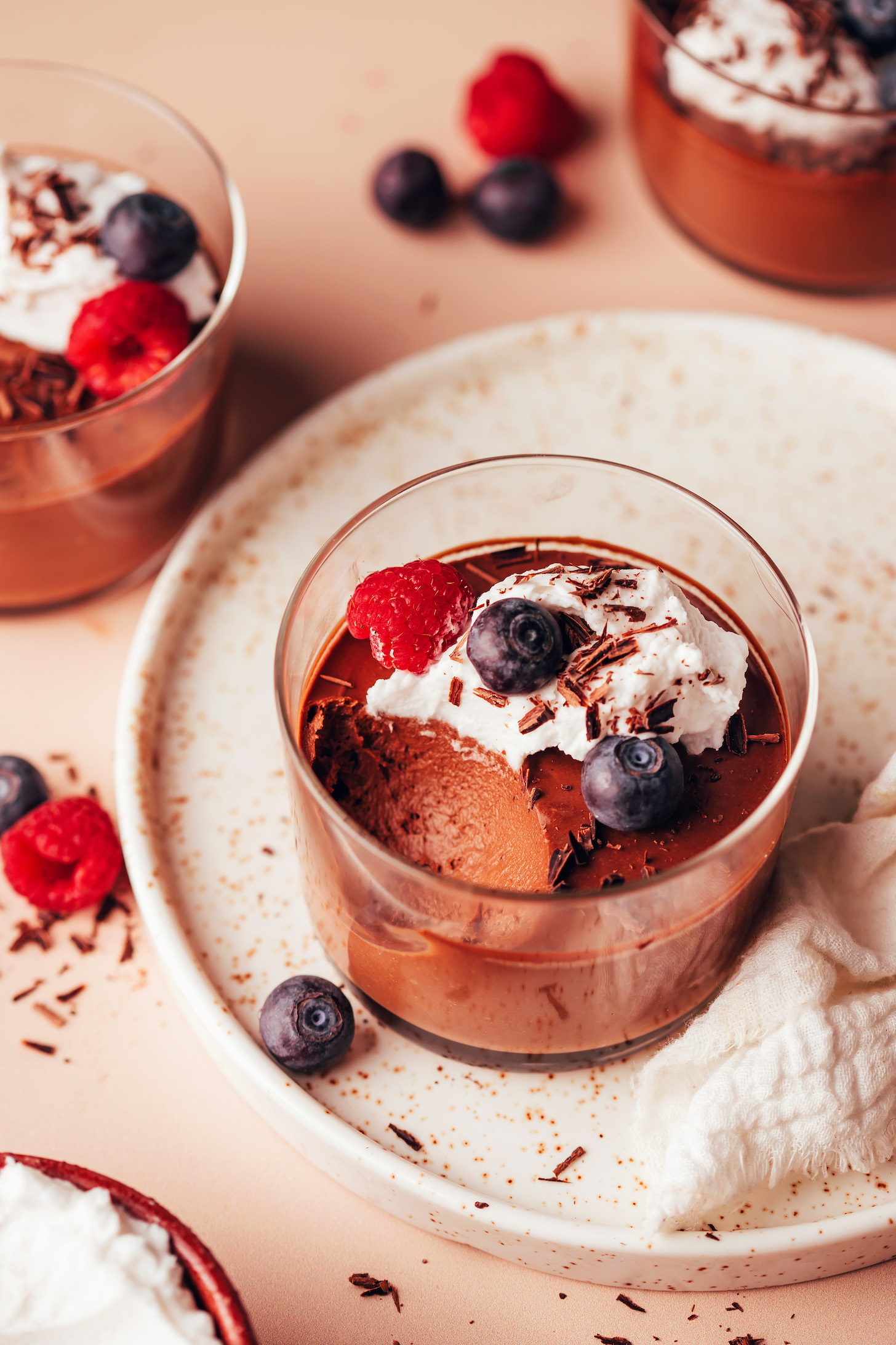 Glasses of vegan chocolate pot de creme topped with coconut whipped cream, berries, and shaved chocolate