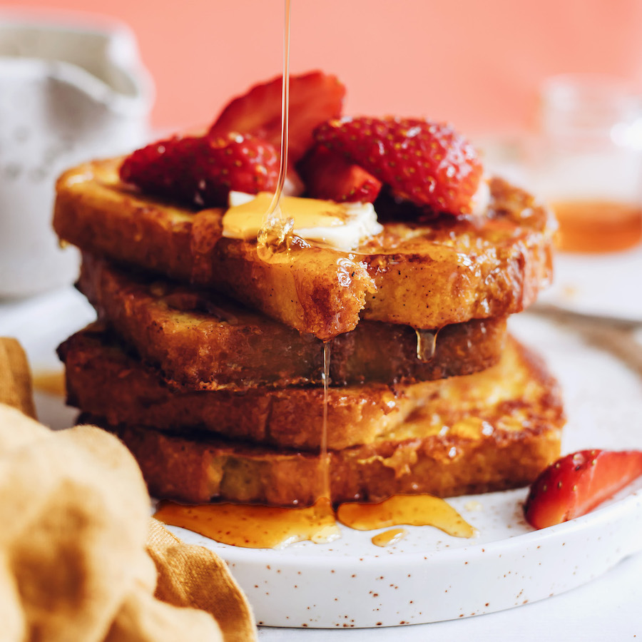 Drizzling maple syrup on slices of vegan French toast with strawberries