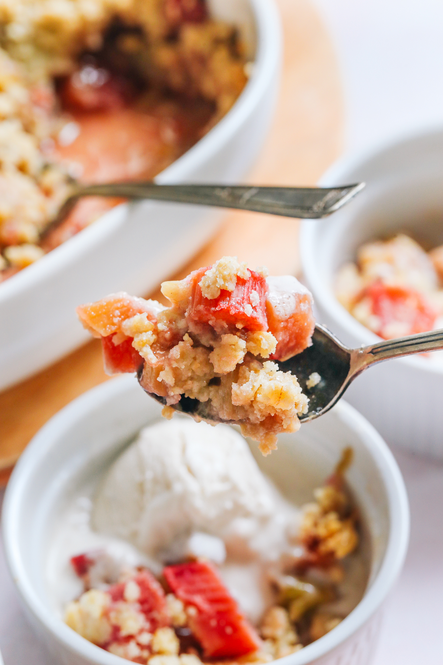 Spoon holding a bite of rhubarb crisp over a bowl