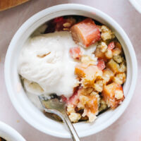 Overhead shot of a bowl of rhubarb crisp topped with a scoop of vanilla ice cream